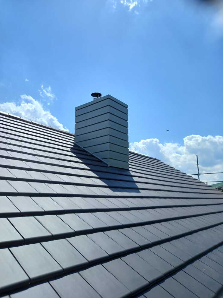 Kaminverkleidung auf Ziegeldach Moderner Schornstein mit Metallverkleidung auf frisch gedecktem Ziegeldach unter blauem Himmel.