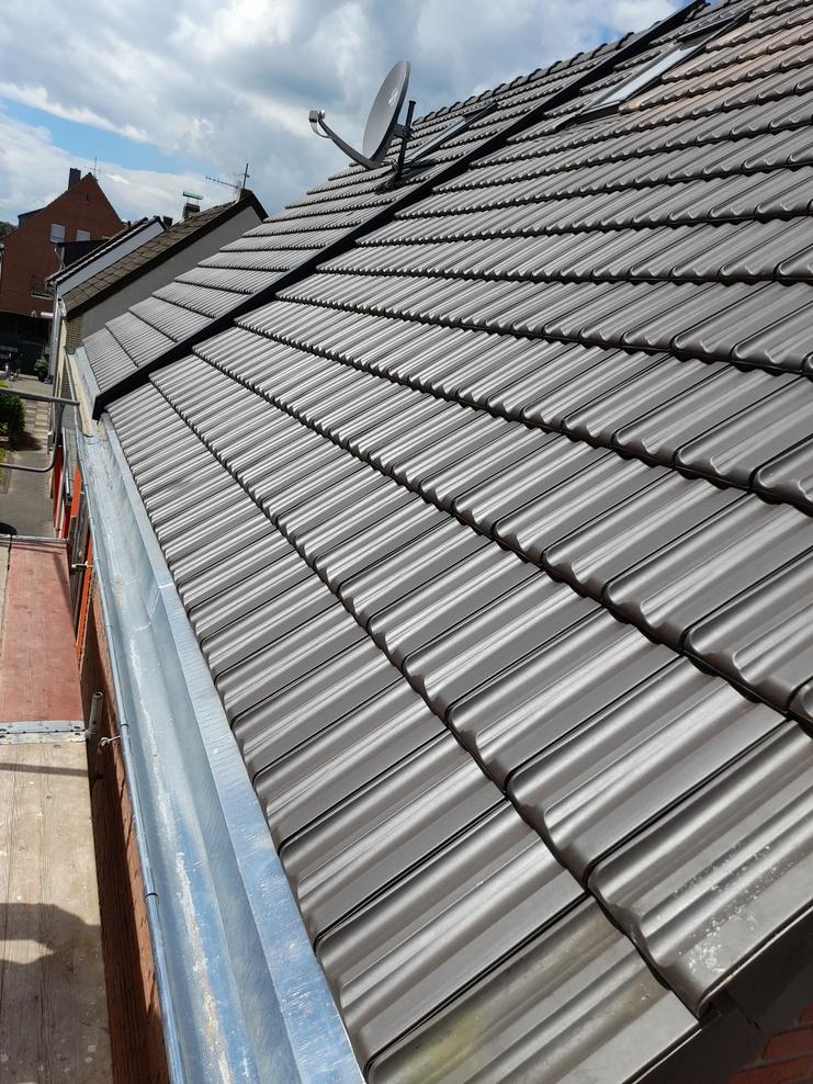 Neu gedecktes Ziegeldach Schrägdach mit neuen dunkelgrauen Dachziegeln, Sat-Schüssel und sauberer Regenrinne.