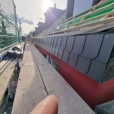 Schieferarbeiten am Dachrand Handwerksarbeiten am Dach mit Schieferplatten und Holzlattung, abgesichert mit Baugerüst.