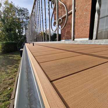 Sanierung Balkonbelag Holzoptik Balkon mit neuem Holzoptik-Belag und verziertem Metallgeländer, montiert durch Dachdeckerbetrieb.