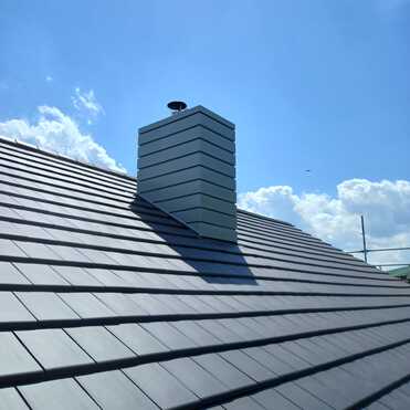 Kaminverkleidung auf Ziegeldach Moderner Schornstein mit Metallverkleidung auf frisch gedecktem Ziegeldach unter blauem Himmel.