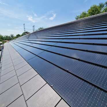 Installation von Solarmodulen auf einem Dach durch eine Bauklempnerei Fachgerechte Montage von Solarmodulen auf einem geneigten Dach durch eine professionelle Bauklempnerei bei sonnigem Wetter.