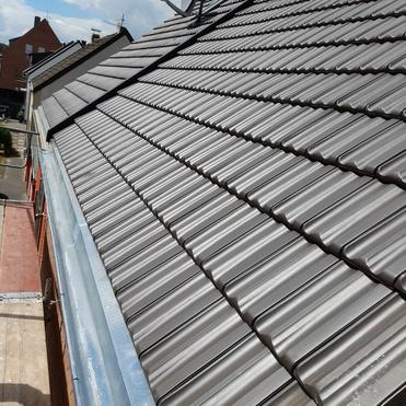Neu gedecktes Ziegeldach Schrägdach mit neuen dunkelgrauen Dachziegeln, Sat-Schüssel und sauberer Regenrinne.