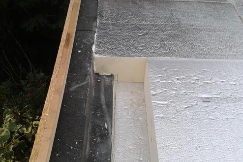 Reparaturbedürftige Dachabdichtung Blick auf einen Teil eines Daches, an dem die Abdichtungsschicht am Rand des Daches beschädigt ist. Der Untergrund ist sichtbar und es gibt Spuren von Verschleiß und Feuchtigkeit.