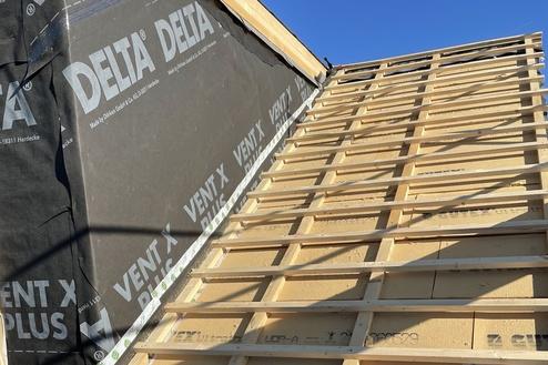 Aufbau eines Daches mit Holzlatten und Dämmmaterial Steilansicht eines Dachaufbaus in der Konstruktionsphase, mit Holzlatten über einer Schicht aus Isoliermaterial. Dämmfolie ist teilweise sichtbar, und die Struktur ist von klarem Himmel beleuchtet.