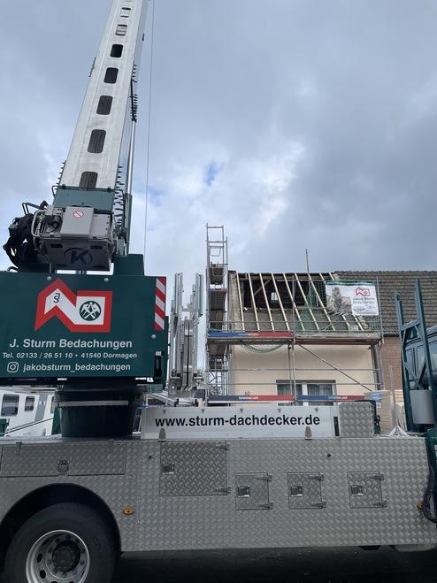 Baustelle mit Kran und Gerüst an einem Haus Ein großer, mobil montierter Kran an einer Baustelle, der vor einem Haus mit Gerüst steht. Der Himmel ist bewölkt.