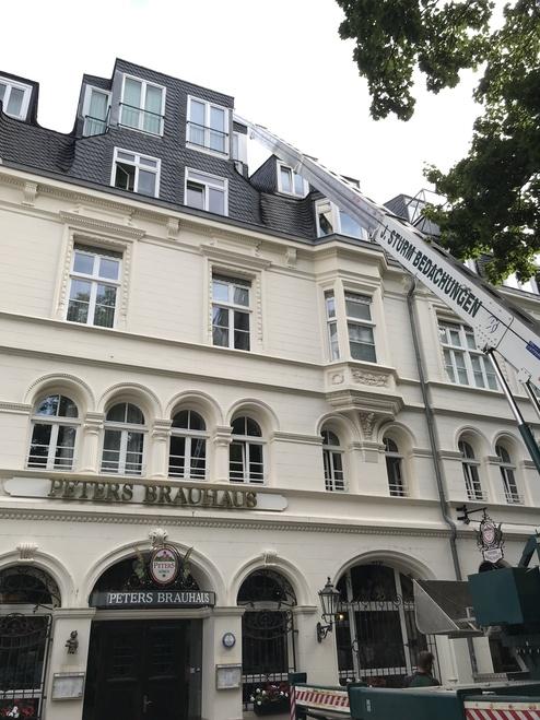 Historisches Brauhaus in der Stadt Außenansicht des "Peters Brauhaus" in einem traditionellen weißen Gebäude mit kunstvollen Fensterrahmungen und dunklem Dach. Eine mobile Hebebühne reicht bis zum Dach.